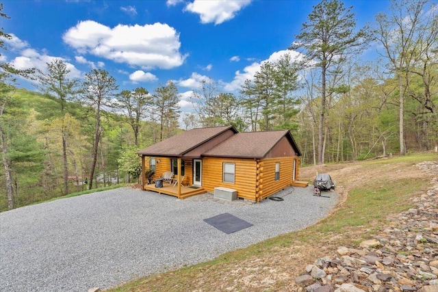 view of front of home featuring log siding, roof with shingles, and a wooded view