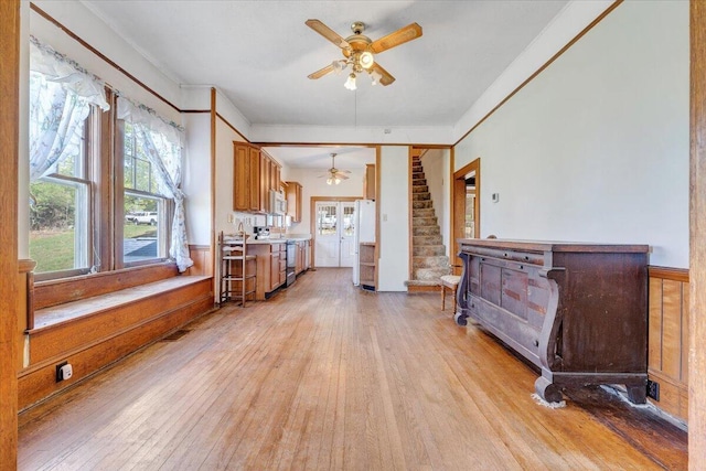 interior space featuring light wood-style flooring, a ceiling fan, ornamental molding, and stairway