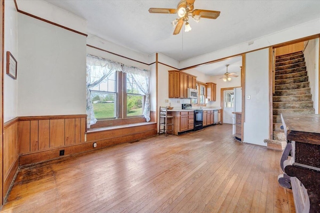 kitchen with light wood finished floors, a ceiling fan, white microwave, wainscoting, and black electric range oven