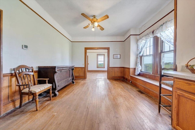 living area featuring wainscoting, ceiling fan, light wood-style flooring, wood walls, and visible vents