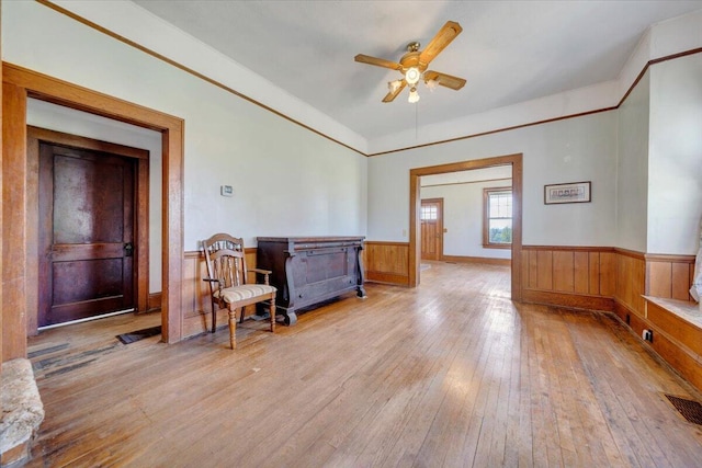 living area with wood walls, visible vents, light wood-style floors, wainscoting, and ceiling fan