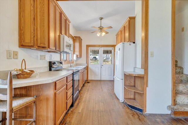 kitchen featuring a ceiling fan, a sink, light wood-style floors, white appliances, and light countertops