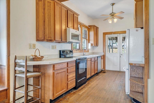 kitchen with a sink, light wood-style flooring, white appliances, ceiling fan, and light countertops