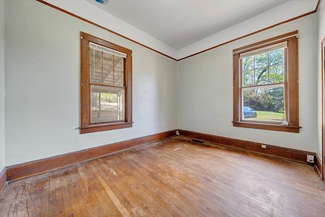 empty room with hardwood / wood-style flooring, baseboards, and visible vents