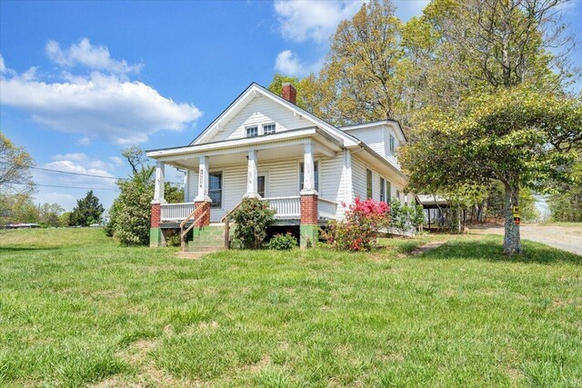 bungalow-style home featuring a chimney, a front lawn, and covered porch
