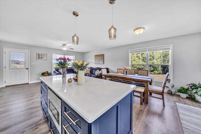 1410 Flowing Springs Rd, Buchanan, VA 24066 - kitchen with light wood-type flooring, light countertops, stainless steel microwave, blue cabinets, and decorative light fixtures