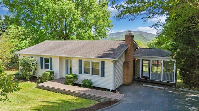 ranch-style house featuring a front yard, a mountain view, a shingled roof, and a chimney