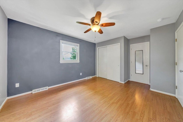 unfurnished bedroom with wood finished floors, visible vents, baseboards, and a closet