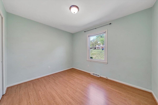 spare room with light wood finished floors, visible vents, and baseboards