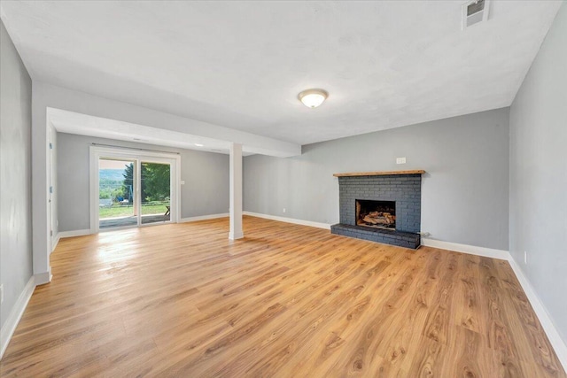 unfurnished living room featuring a brick fireplace, light wood finished floors, visible vents, and baseboards