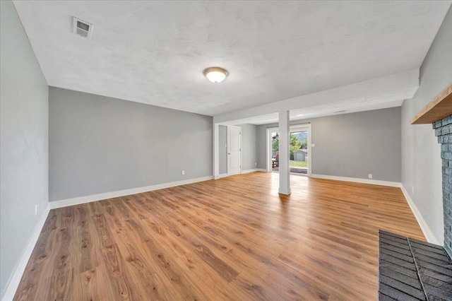 unfurnished living room featuring baseboards, visible vents, light wood-style floors, and a brick fireplace