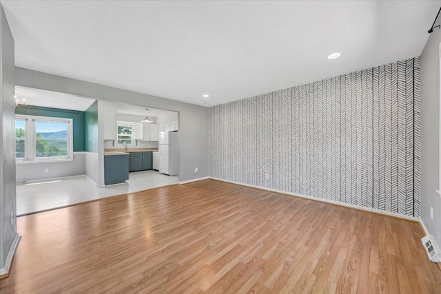 unfurnished living room with baseboards, an accent wall, wallpapered walls, and light wood-style flooring