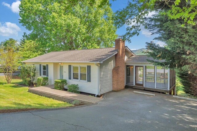 ranch-style house featuring a sunroom, roof with shingles, a front yard, and a chimney