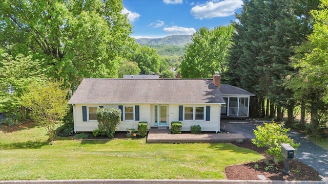 ranch-style house with a sunroom, a mountain view, a front yard, and a chimney