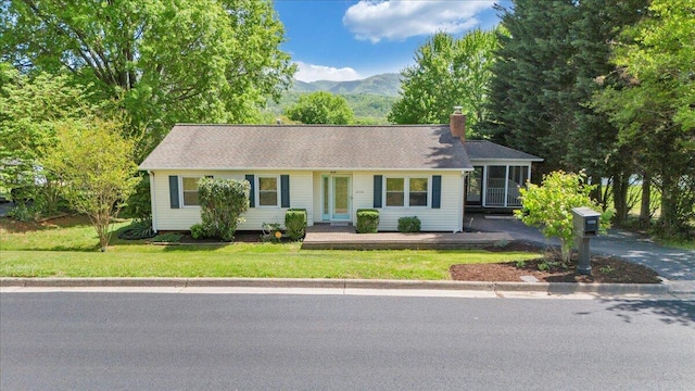 single story home featuring a chimney, a front yard, a mountain view, and a sunroom