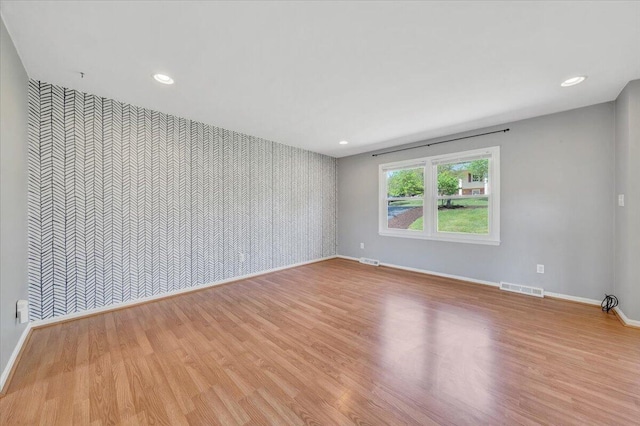 unfurnished room with an accent wall, wood finished floors, wallpapered walls, and baseboards