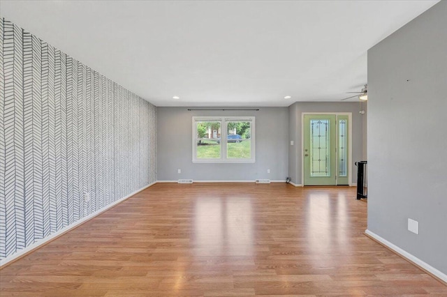 unfurnished living room featuring wallpapered walls, an accent wall, light wood-type flooring, baseboards, and visible vents