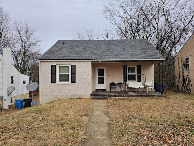 bungalow featuring a porch, roof with shingles, stucco siding, and a front yard
