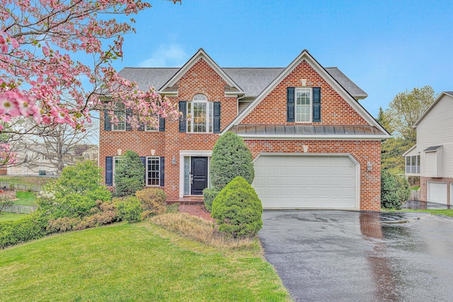 traditional home featuring a front yard, a shingled roof, aphalt driveway, brick siding, and an attached garage