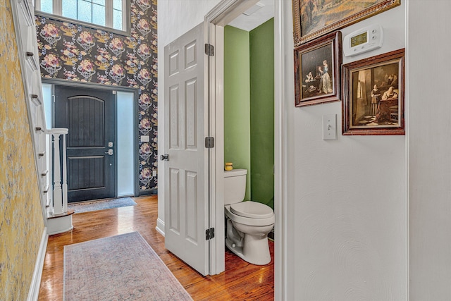 bathroom featuring wood finished floors, toilet, wallpapered walls, and baseboards