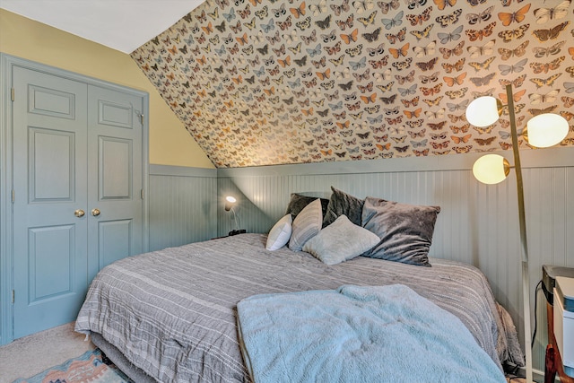 bedroom with lofted ceiling, a wainscoted wall, wallpapered walls, a closet, and carpet