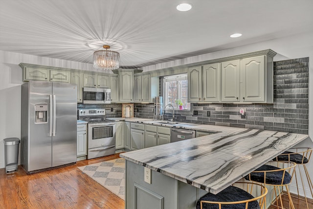 kitchen featuring decorative backsplash, stainless steel appliances, a sink, a notable chandelier, and a peninsula