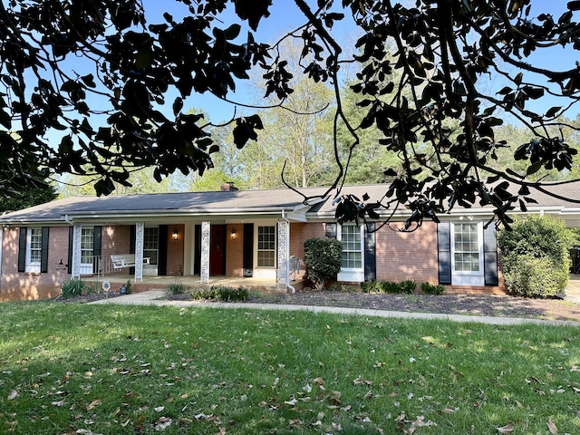 view of front of home featuring a chimney, a front lawn, brick siding, and covered porch