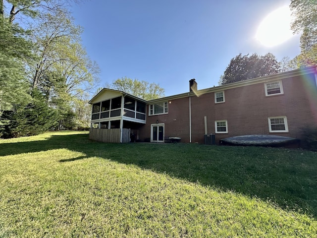 back of property with central AC, a chimney, brick siding, a yard, and a sunroom