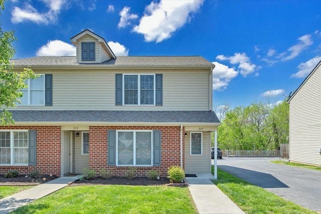 view of front of property with a front yard, roof with shingles, brick siding, and fence