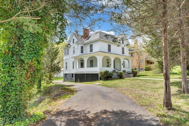 view of front of house featuring a porch, a front lawn, and a chimney