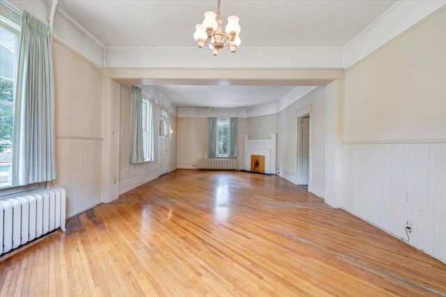 unfurnished living room with radiator, a wainscoted wall, an inviting chandelier, and light wood-type flooring