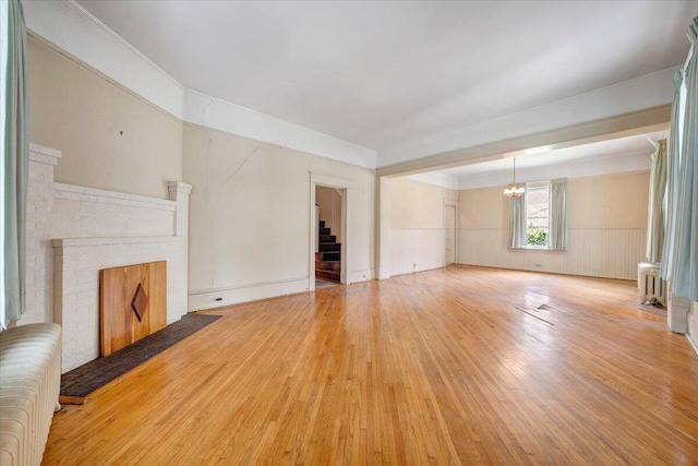 unfurnished living room featuring an inviting chandelier, light wood finished floors, a brick fireplace, radiator heating unit, and stairs