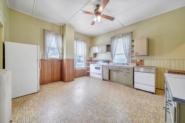 kitchen with a sink, white appliances, a wainscoted wall, a ceiling fan, and light countertops
