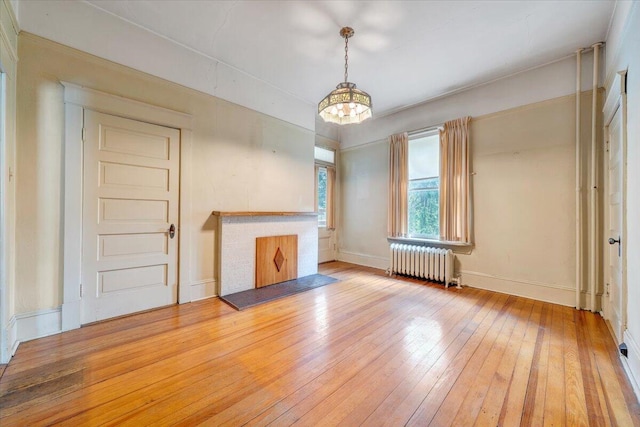 unfurnished living room featuring radiator, an inviting chandelier, baseboards, and light wood-type flooring