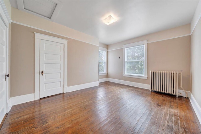 empty room with attic access, hardwood / wood-style flooring, baseboards, and radiator
