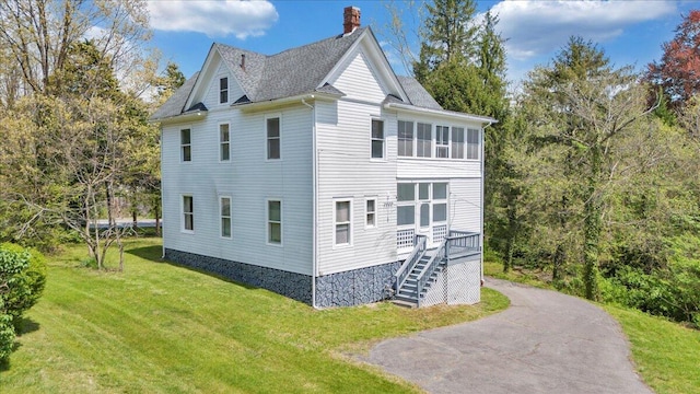 view of property exterior featuring roof with shingles, a chimney, a yard, and stairs
