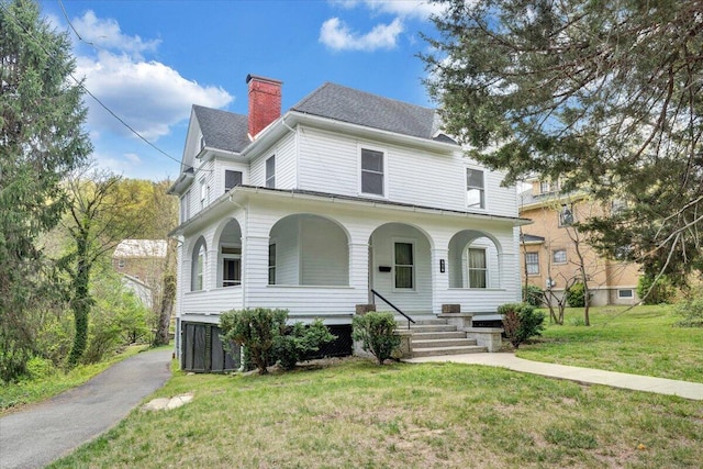 view of front of house with covered porch, a shingled roof, a chimney, and a front lawn