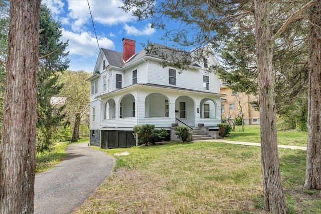 view of front of house with a porch, a front yard, and a chimney