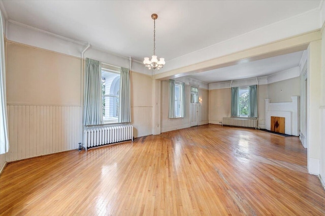 unfurnished living room with a chandelier, wainscoting, radiator, and wood-type flooring