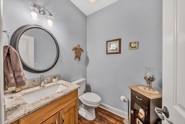 half bathroom with toilet, vanity, wood finished floors, and baseboards