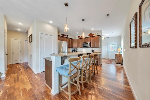 kitchen with appliances with stainless steel finishes, wood finished floors, baseboards, a kitchen island with sink, and recessed lighting