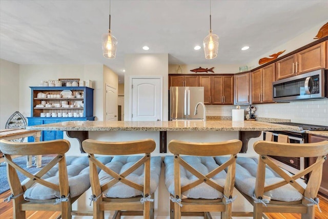 kitchen featuring stainless steel appliances, a breakfast bar, light stone countertops, backsplash, and recessed lighting