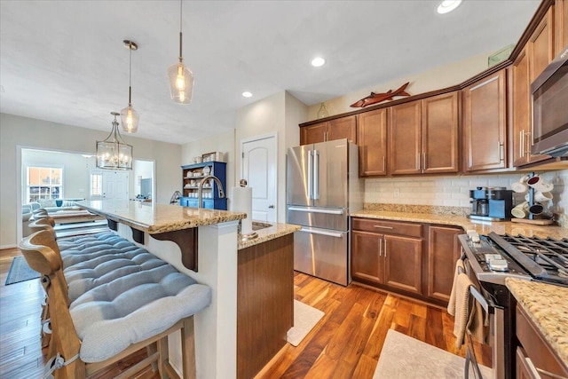 kitchen with appliances with stainless steel finishes, a sink, light wood-type flooring, tasteful backsplash, and a kitchen breakfast bar