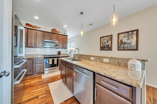 kitchen featuring stainless steel appliances, a sink, light wood-type flooring, a center island with sink, and hanging light fixtures