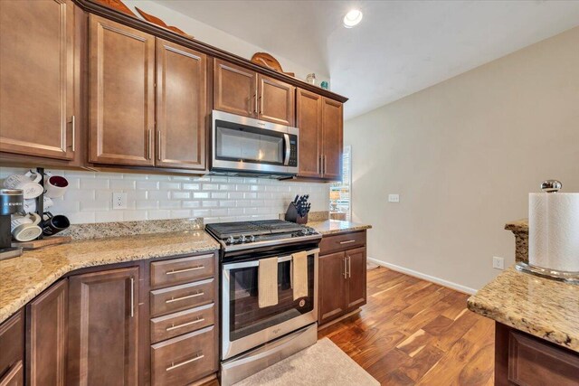 kitchen with stainless steel appliances, tasteful backsplash, dark wood finished floors, baseboards, and light stone countertops