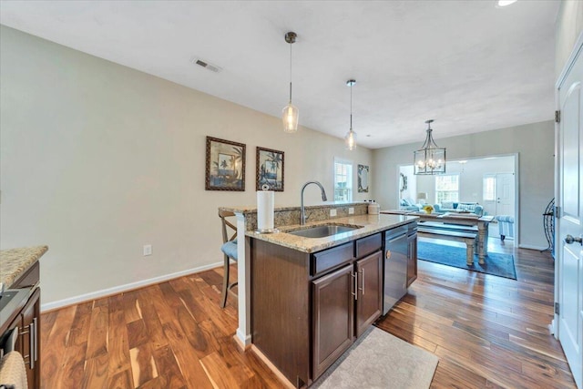 kitchen with a sink, dishwasher, dark wood finished floors, pendant lighting, and light stone countertops