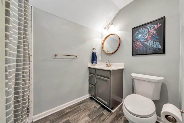 bathroom with lofted ceiling, toilet, wood finish floors, vanity, and baseboards