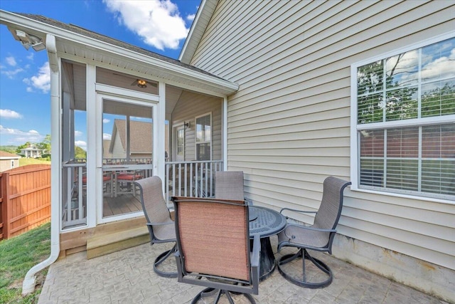view of patio with outdoor dining space, fence, and a sunroom