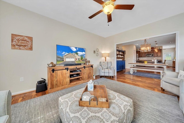 living area with a chandelier, wood finished floors, a ceiling fan, and baseboards