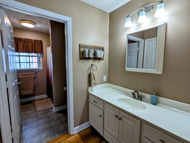 full bath with baseboards, vanity, and a textured ceiling
